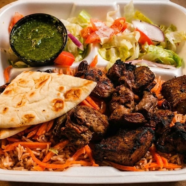 Grilled meat with rice, carrots, flatbread, green sauce, and salad in a takeout container.