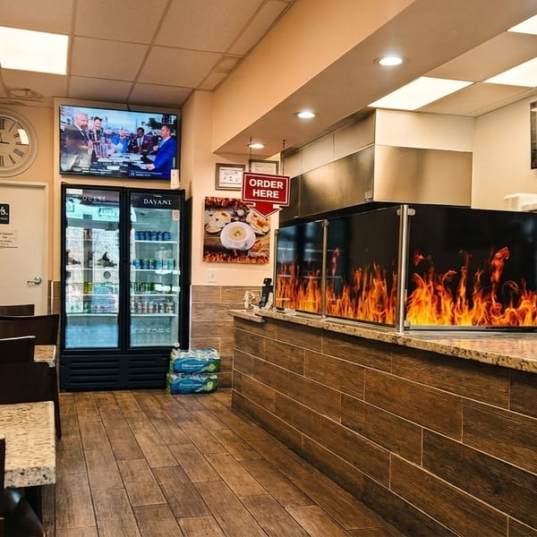 Interior of a casual restaurant with tables, a counter with a flame-patterned screen, and a menu board.