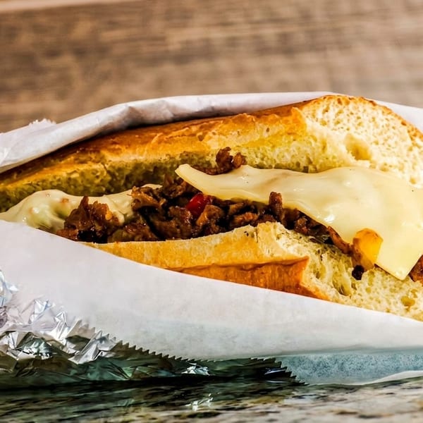 Cheesesteak sandwich with melted cheese, steak, and peppers, wrapped in paper and foil.