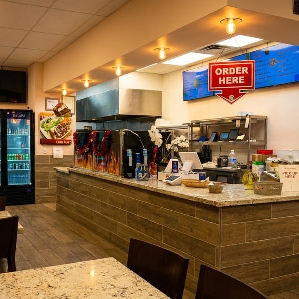 Interior of a casual restaurant with empty tables, a service counter, and a menu board.