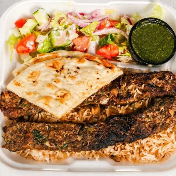 Two grilled kebabs on rice with naan bread, a side salad, and green sauce in a takeout container.